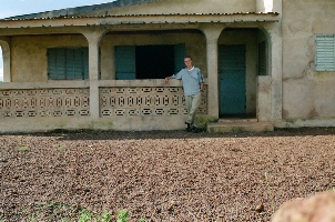 Jeremy Gernand standing in front of the house where he lived 
			during his service as a Peace Corps Volunteer between 1998 and 2000.